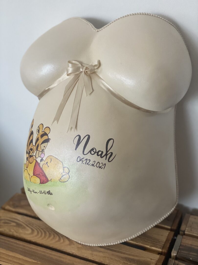 Babybauch-Gipsabdruck mit cremefarbener Schleife und persönlicher Gestaltung