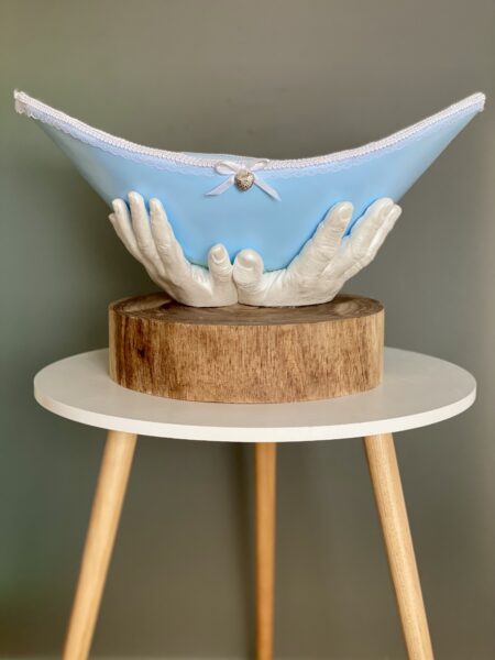 Blaue Belly Bowl mit weißer Spitze und den Händen der Eltern als Sockel auf einem runden Holzsockel