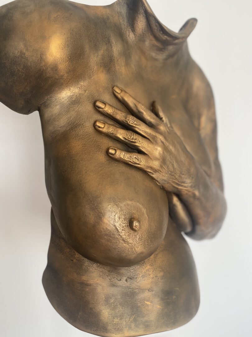 Detailansicht eines bronzefarbenen Oberkörperabdrucks mit Hand auf dem Brustbein