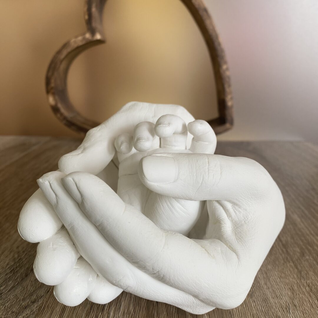 Mama und Papa halten die Hand ihres Kindes als detailgetreuen Gipsabdruck gemeinsam in ihren Händen