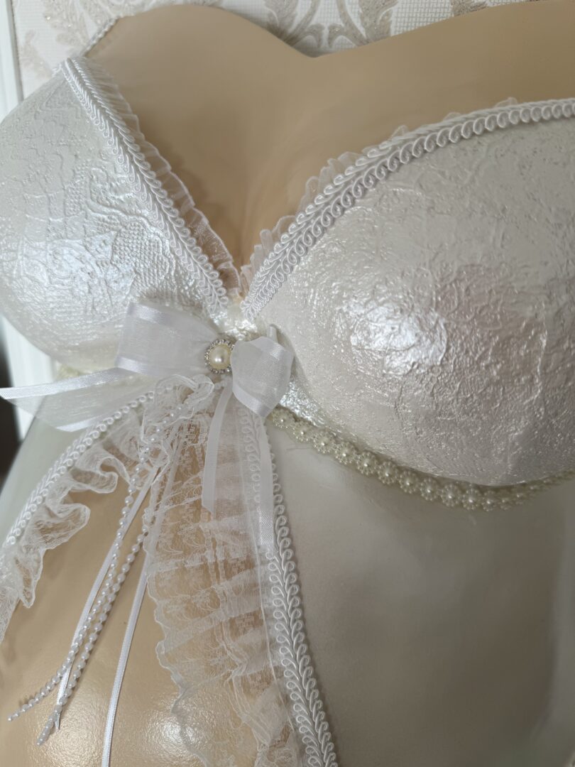 Detailaufnahme eines romantisch veredelten Babybauch Gipsabdrucks mit weißer Spitzen-BH-Optik und Schleife