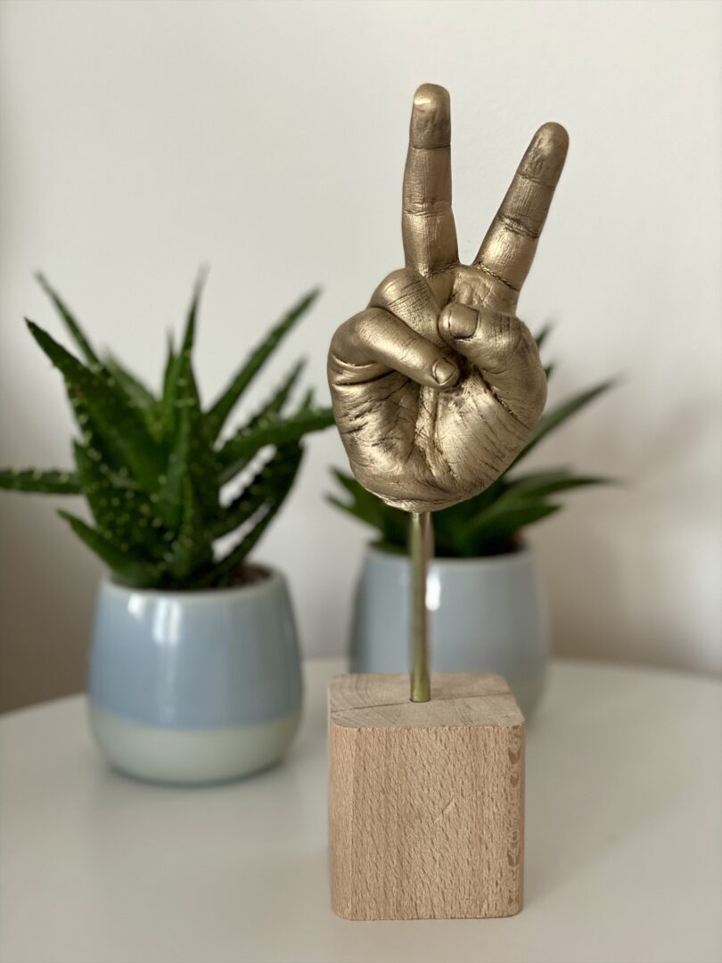 Detailgetreuer Gipsabdruck einer Kinderhand in Antikgold mit erhobenen Fingern auf einem Holzsockel