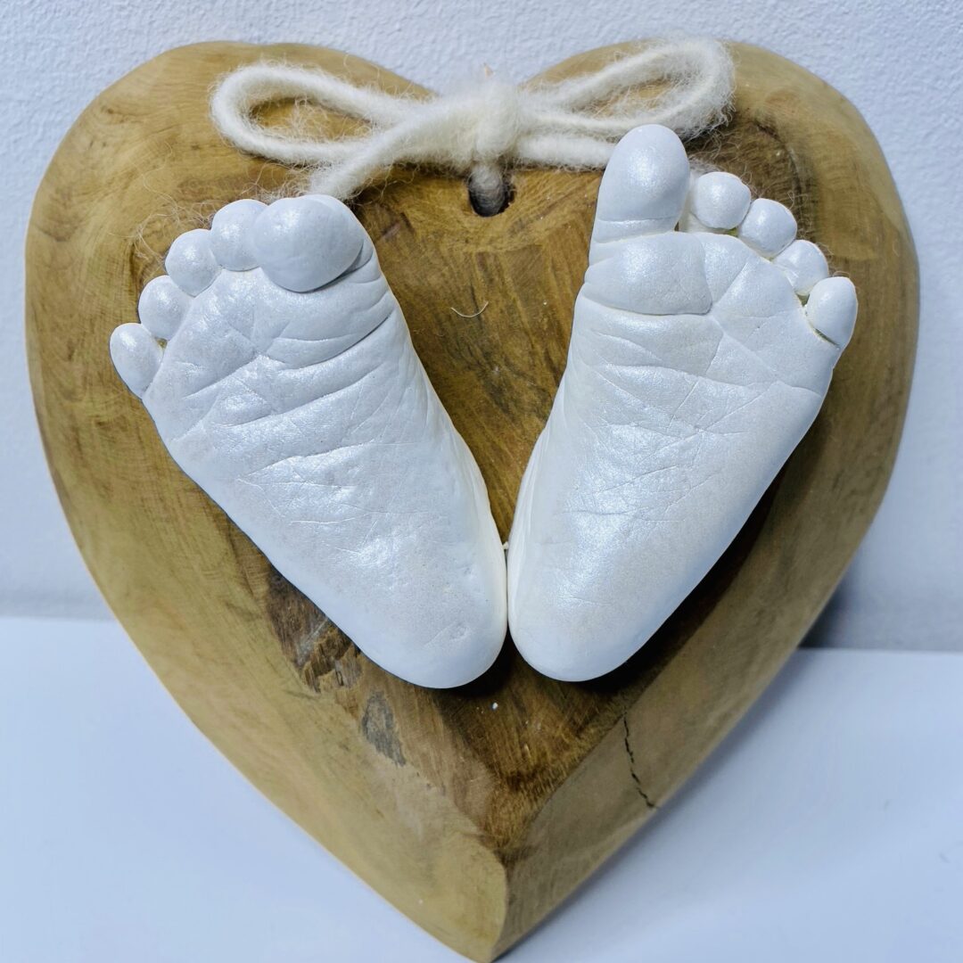 Babyfüße als detailgetreue Gipsabformungen auf einem natürlichen Holzherz mit Schleife