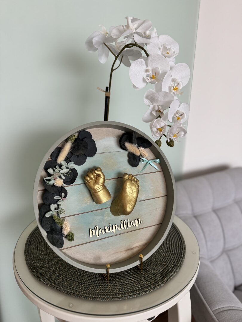 Goldener Gipsabdruck von Babyhand und Babyfuß in einem runden Rahmen mit Eukalyptus und Trockenblumen