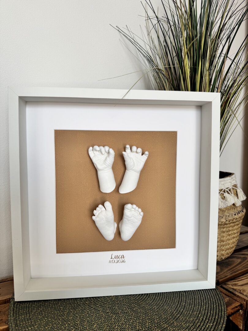 Hände und Füße eines neugeborenen Babys als detailgetreue Gipsabdrücke in einem weißen Rahmen