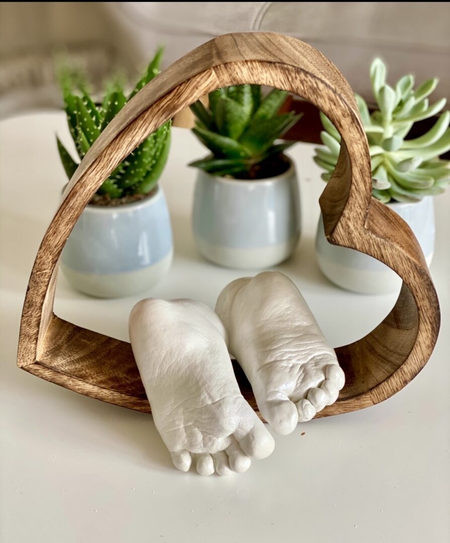 Detailgetreue Gipsabdrücke von Babyfüßen, liegend in einem natürlichen Holzherz