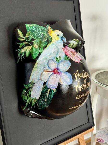 Babybauch Gipsabdruck mit handgemalten Blumen und Papagei im schwarzen Rahmen