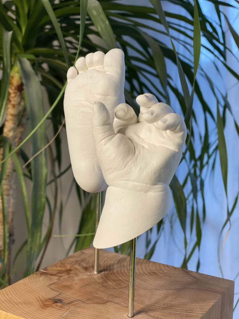 Detailaufnahme von Babyhänden und Babyfüßen als Gipsabformung auf einem schweren Eichenholzsockel